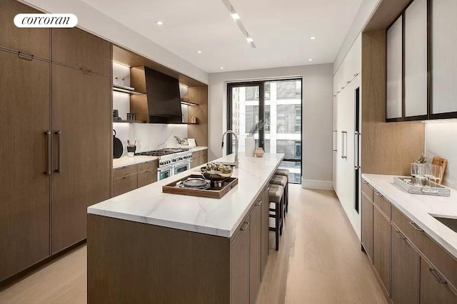 kitchen featuring a kitchen breakfast bar, double oven range, a kitchen island with sink, and light hardwood / wood-style floors