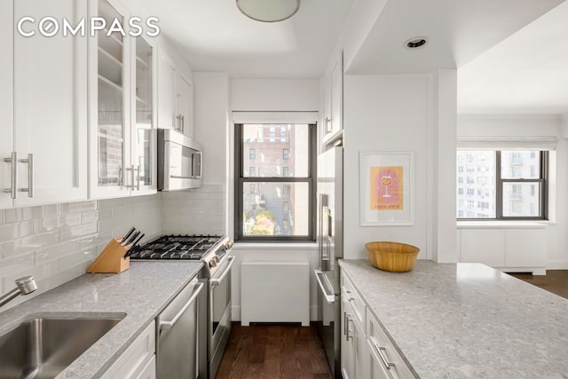 kitchen with appliances with stainless steel finishes, white cabinets, a sink, and backsplash