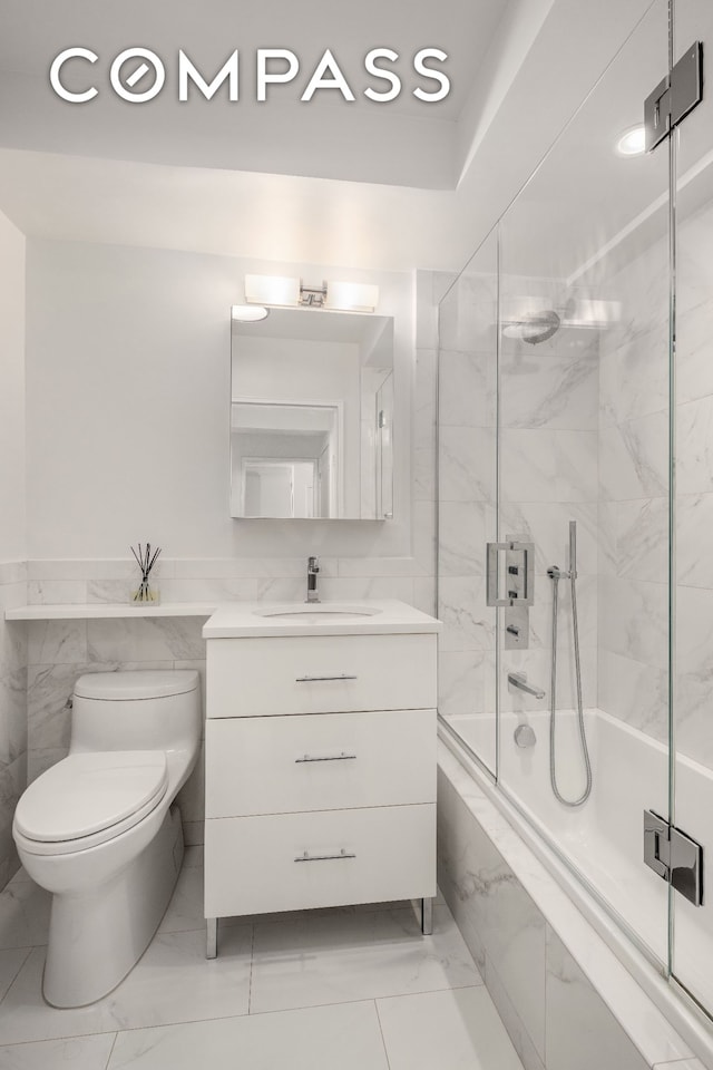 full bathroom with marble finish floor, shower / bath combination with glass door, tile walls, toilet, and vanity