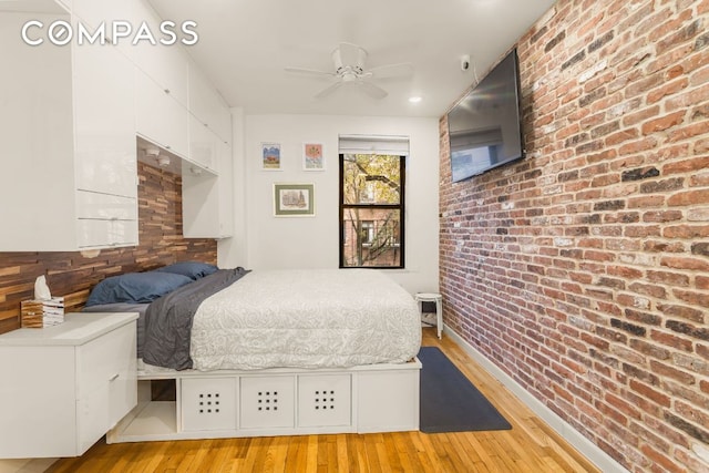 bedroom with ceiling fan, brick wall, and light hardwood / wood-style flooring