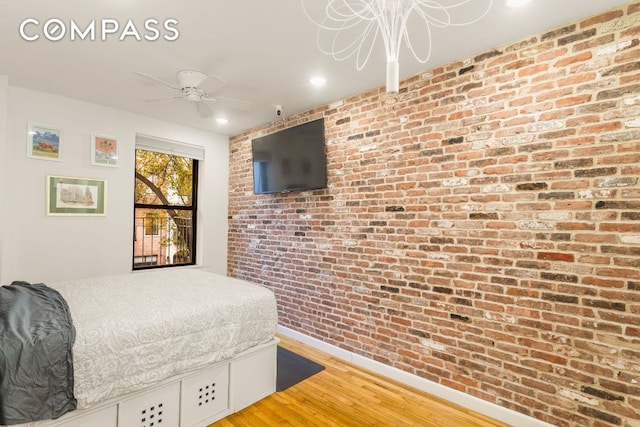 bedroom with ceiling fan, brick wall, and light hardwood / wood-style floors