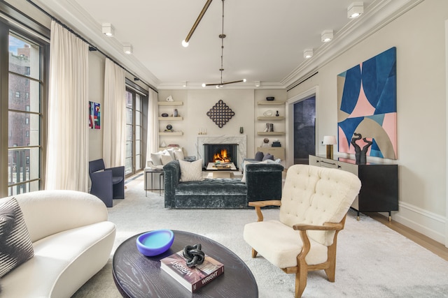 living area featuring built in shelves, wood finished floors, baseboards, a lit fireplace, and crown molding