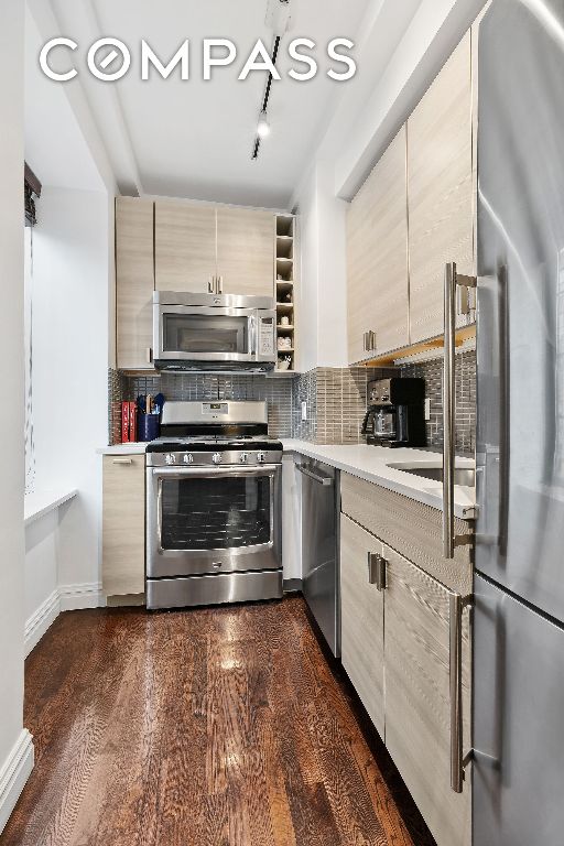 kitchen with tasteful backsplash, dark hardwood / wood-style flooring, light brown cabinets, and appliances with stainless steel finishes