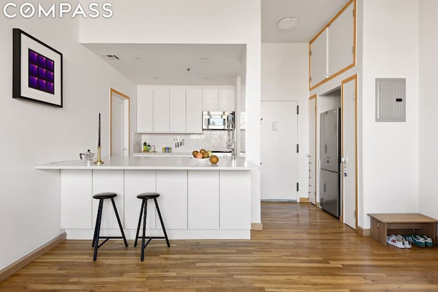 kitchen featuring a breakfast bar, white cabinets, decorative backsplash, electric panel, and kitchen peninsula