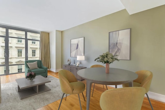 interior space with a wealth of natural light, a wall of windows, light wood-style flooring, and baseboards