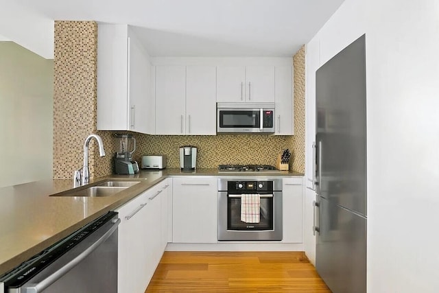 kitchen with light wood finished floors, backsplash, appliances with stainless steel finishes, and a sink