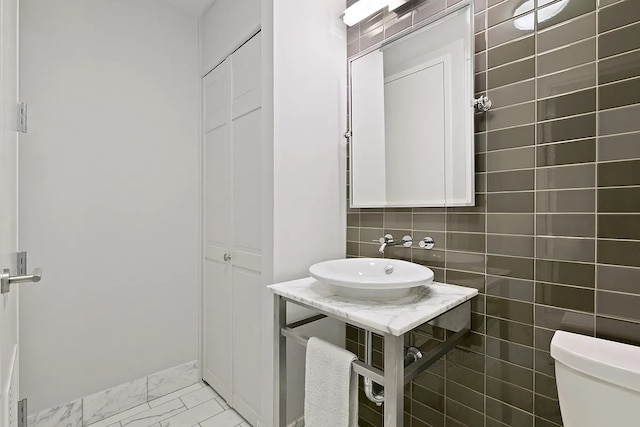 half bath with toilet, marble finish floor, tasteful backsplash, baseboards, and vanity