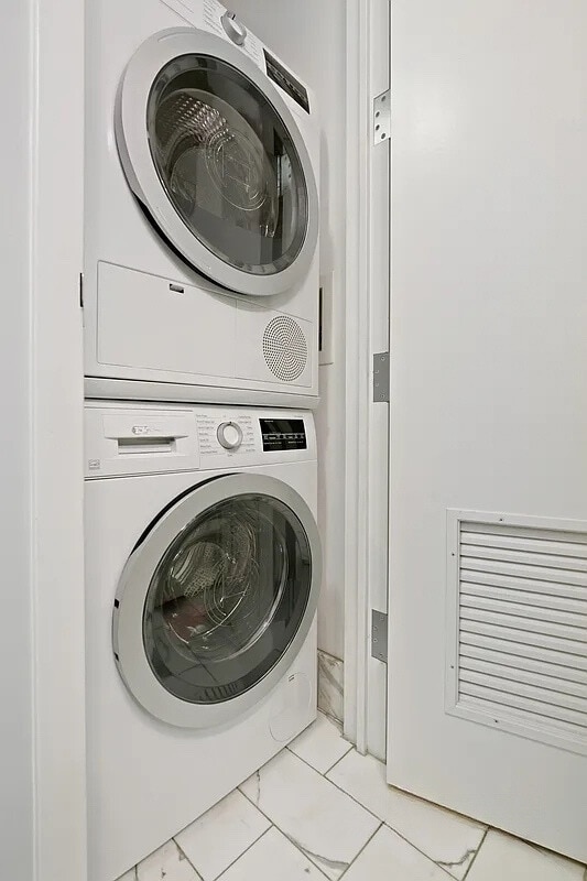 clothes washing area featuring laundry area, stacked washer / drying machine, and marble finish floor