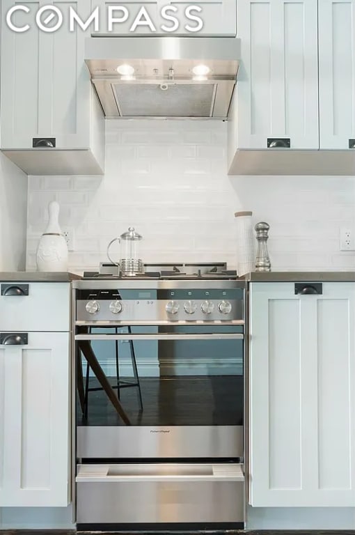 kitchen featuring tasteful backsplash, ventilation hood, white cabinetry, and stainless steel stove