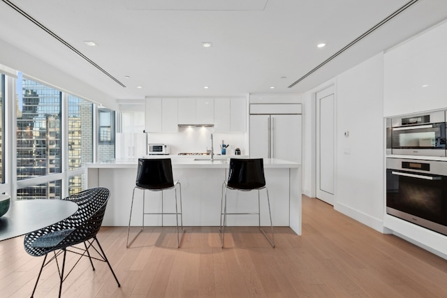 kitchen featuring white microwave, modern cabinets, a breakfast bar, light countertops, and white cabinetry