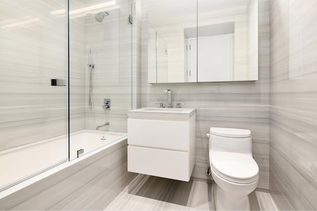 bathroom with enclosed tub / shower combo, vanity, toilet, and tile walls