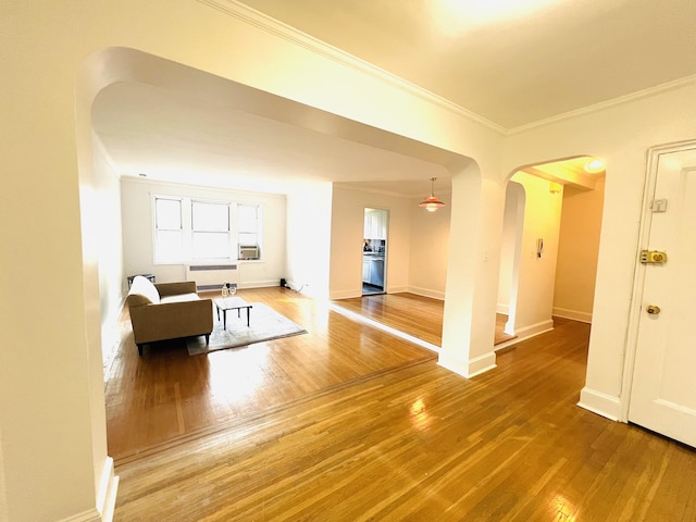 unfurnished living room with baseboards, ornamental molding, arched walkways, and wood finished floors