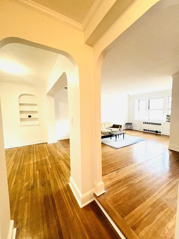 hallway with ornamental molding, radiator, and hardwood / wood-style flooring