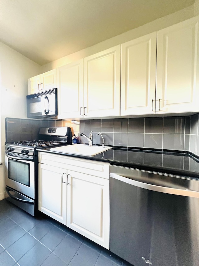 76-15 35th Ave Unit 5-H, New York City, NY 11372 - kitchen with stainless steel appliances, a sink, white cabinetry, backsplash, and dark tile patterned flooring