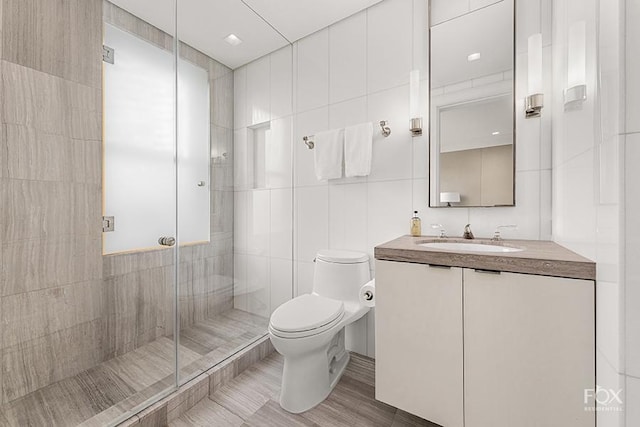 full bath featuring toilet, a stall shower, vanity, and tile walls