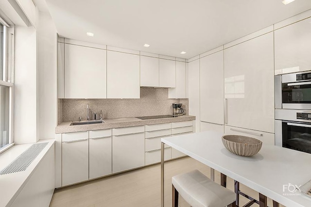 kitchen with sink, backsplash, white cabinets, stainless steel double oven, and black electric cooktop