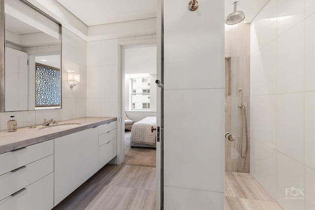 ensuite bathroom featuring connected bathroom, wood finished floors, a tile shower, vanity, and tile walls