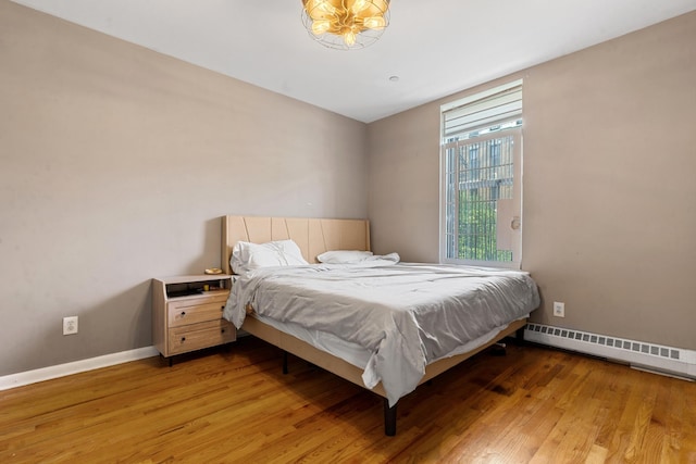 bedroom with a baseboard heating unit, light wood-style flooring, and baseboards