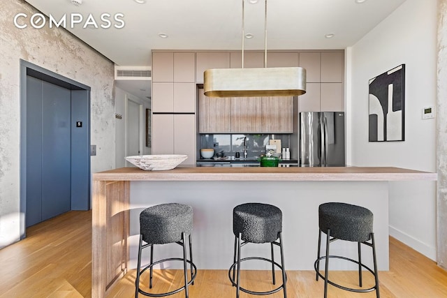 kitchen featuring light hardwood / wood-style flooring, gray cabinets, stainless steel refrigerator, a breakfast bar, and elevator