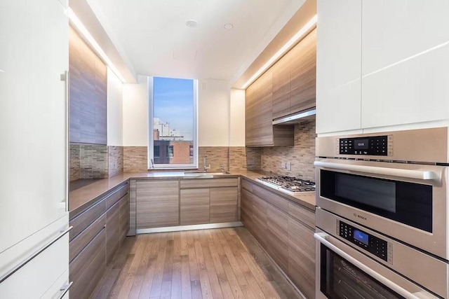 kitchen featuring hardwood / wood-style floors, stainless steel appliances, decorative backsplash, white cabinets, and sink