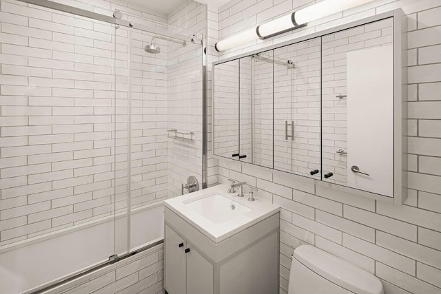 full bathroom featuring bath / shower combo with glass door, tile walls, vanity, and toilet