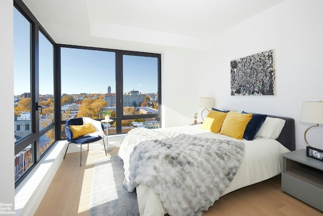 bedroom with a view of city, a wall of windows, and wood finished floors