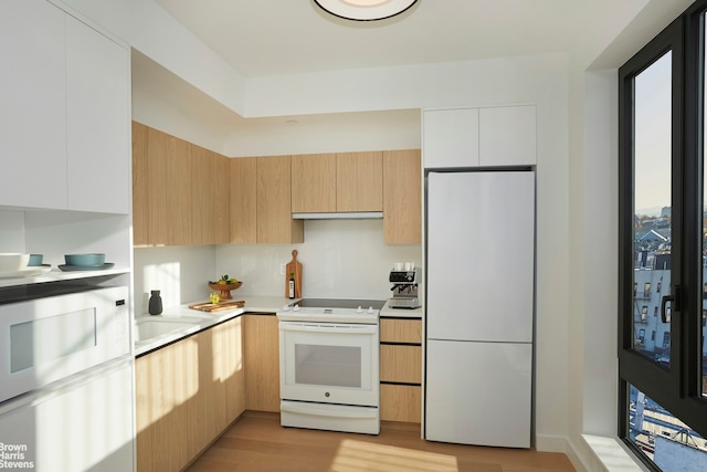 kitchen with modern cabinets, light countertops, under cabinet range hood, white appliances, and light wood-style flooring