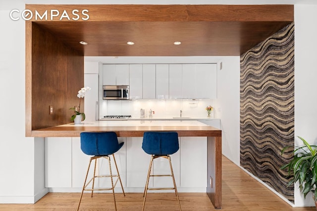 kitchen with modern cabinets, stainless steel microwave, a breakfast bar area, light countertops, and white cabinetry