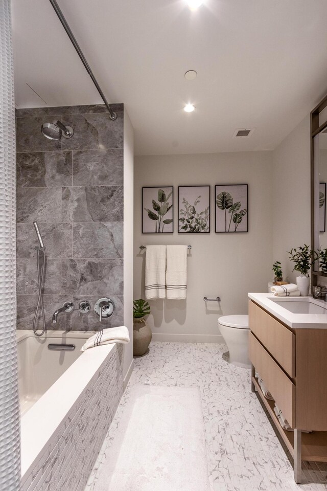 full bathroom featuring toilet, tiled shower / bath combo, vanity, visible vents, and baseboards