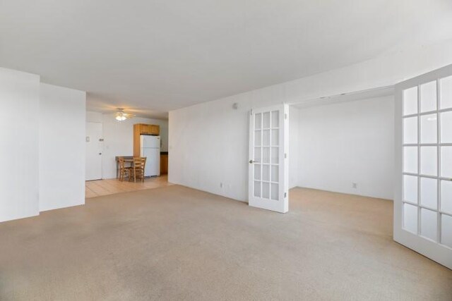 empty room with ceiling fan, light colored carpet, and french doors