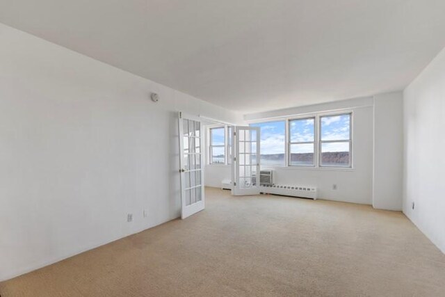 empty room with a baseboard radiator, light colored carpet, french doors, and a wall mounted air conditioner