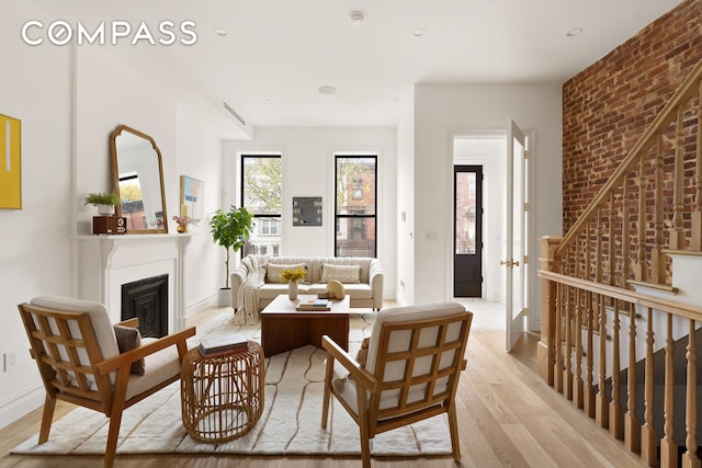 living area with brick wall, baseboards, recessed lighting, a fireplace, and light wood-style floors