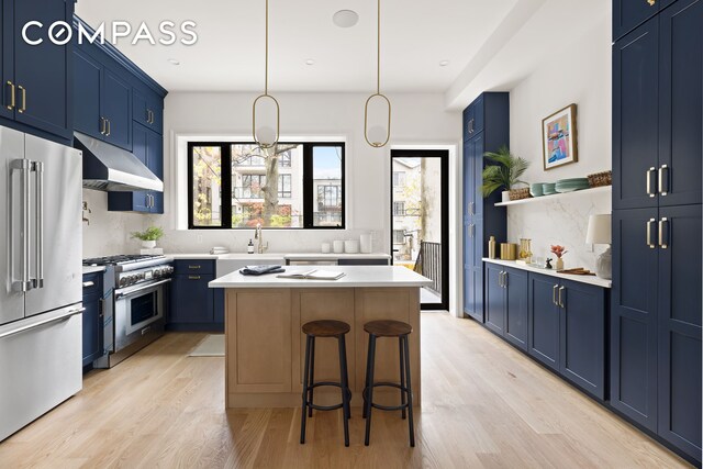 kitchen featuring under cabinet range hood, premium appliances, a center island, and blue cabinets