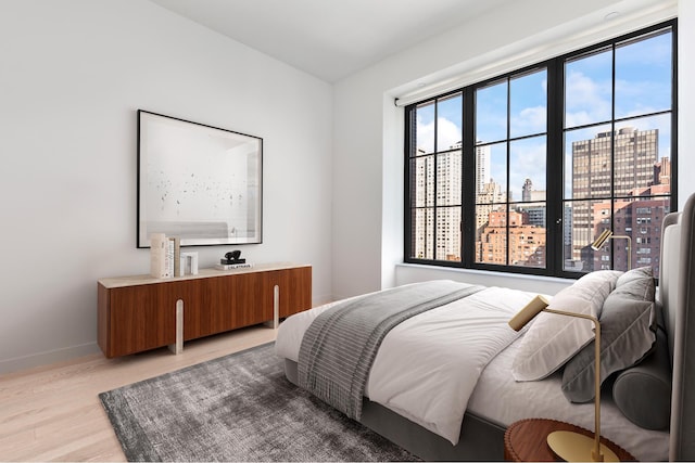 bedroom with light wood-type flooring, baseboards, and a city view