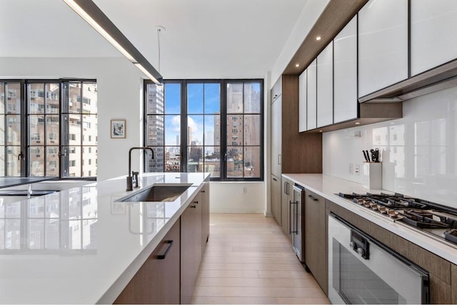 kitchen featuring stainless steel gas stovetop, sink, wall oven, white cabinets, and beverage cooler