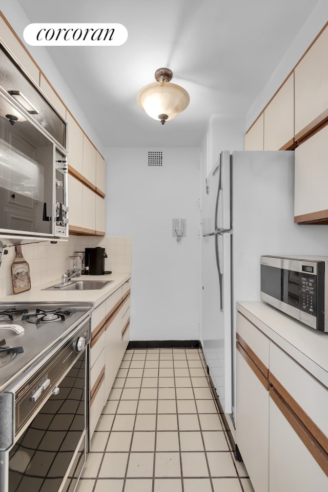 kitchen featuring stainless steel microwave, light countertops, decorative backsplash, range, and a sink