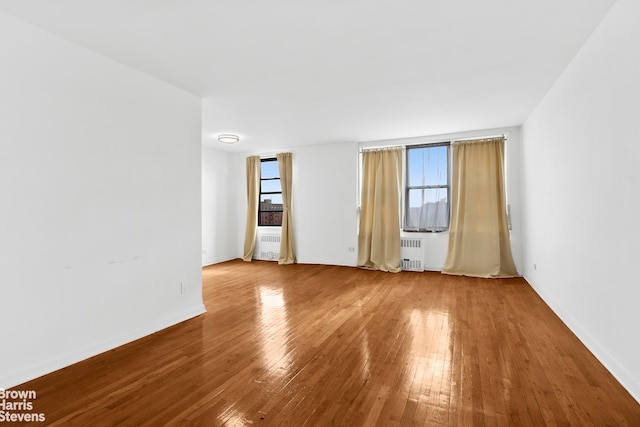 empty room featuring baseboards, hardwood / wood-style floors, and radiator heating unit