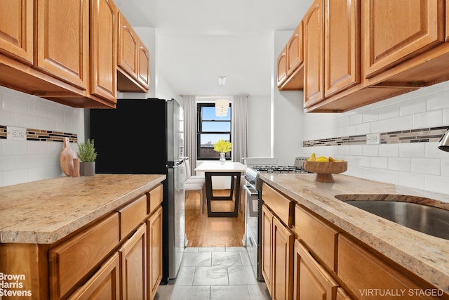 kitchen featuring tasteful backsplash, range with gas stovetop, brown cabinets, freestanding refrigerator, and a sink