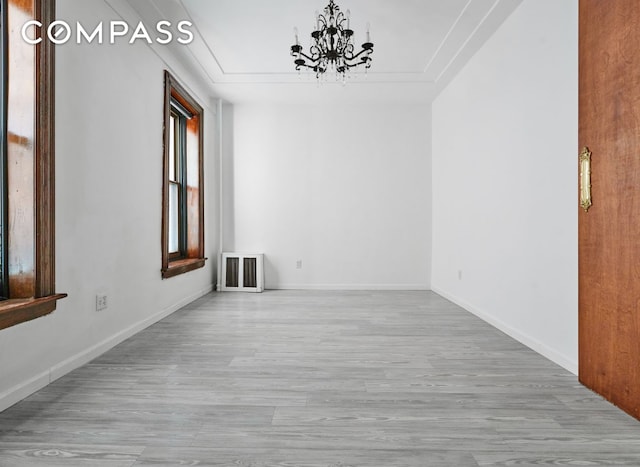 unfurnished room featuring an inviting chandelier, a tray ceiling, and light hardwood / wood-style floors