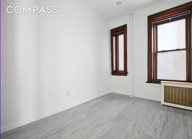 spare room with radiator, light wood-style flooring, and baseboards