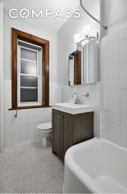 bathroom with toilet, vanity, tile walls, wainscoting, and tile patterned floors