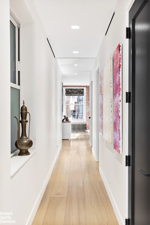 hall featuring radiator, light wood-style floors, and baseboards