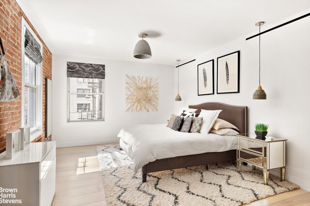 bedroom with light wood-style floors, baseboards, and brick wall