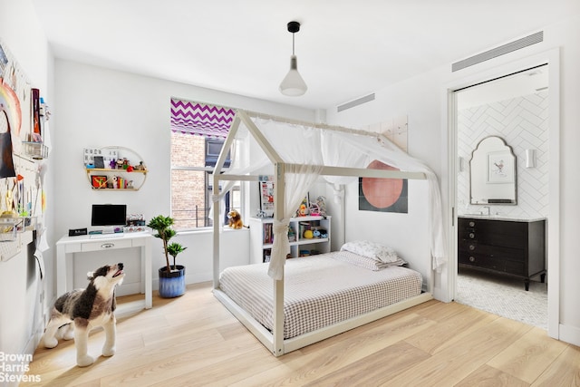 bedroom featuring wood finished floors, visible vents, and connected bathroom