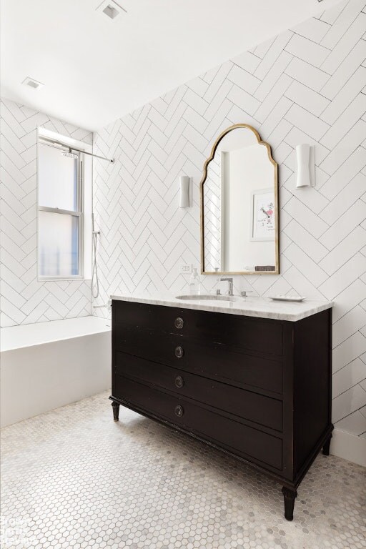 bathroom with a tub to relax in, visible vents, tile walls, and vanity