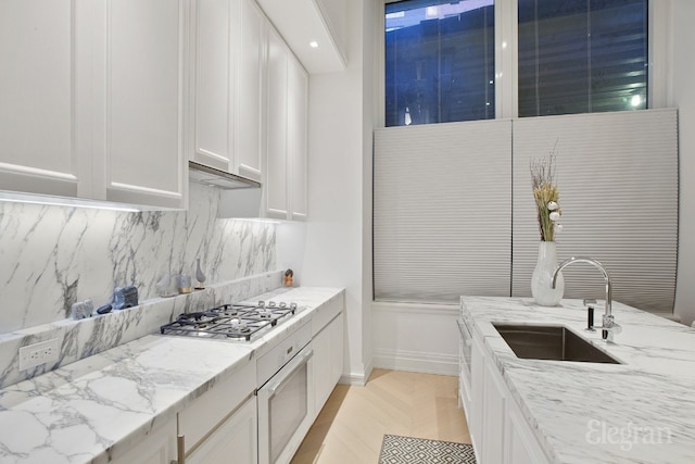 interior space with light stone counters, stainless steel gas stovetop, sink, and white cabinets