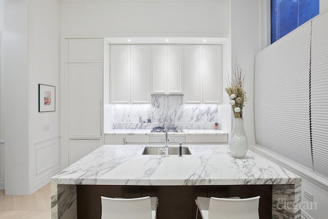 kitchen with sink, a breakfast bar area, white cabinetry, light stone counters, and tasteful backsplash