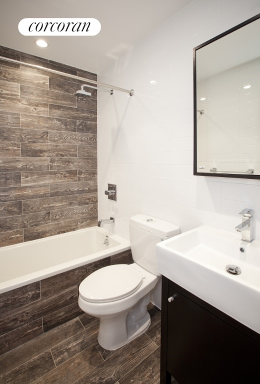 full bathroom featuring toilet, tile walls, vanity, and tiled shower / bath combo