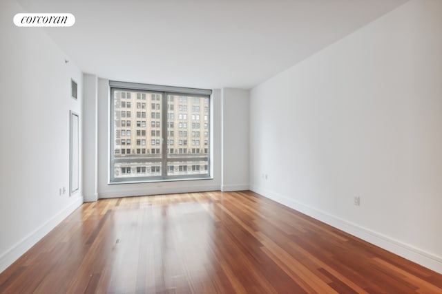 spare room with wood finished floors, visible vents, and baseboards