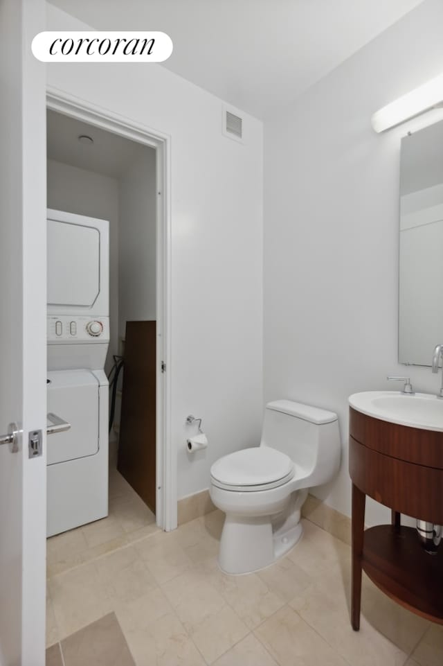 bathroom with stacked washing machine and dryer, toilet, vanity, and baseboards